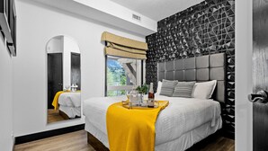 Een moderne slaapkamer met een groot bed, een spiegel, een raam met uitzicht en een wand met een geometrisch patroon.