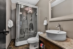 A modern bathroom with a glass-enclosed shower, a white toilet, a sink with a marble countertop, and a large mirror above the sink.