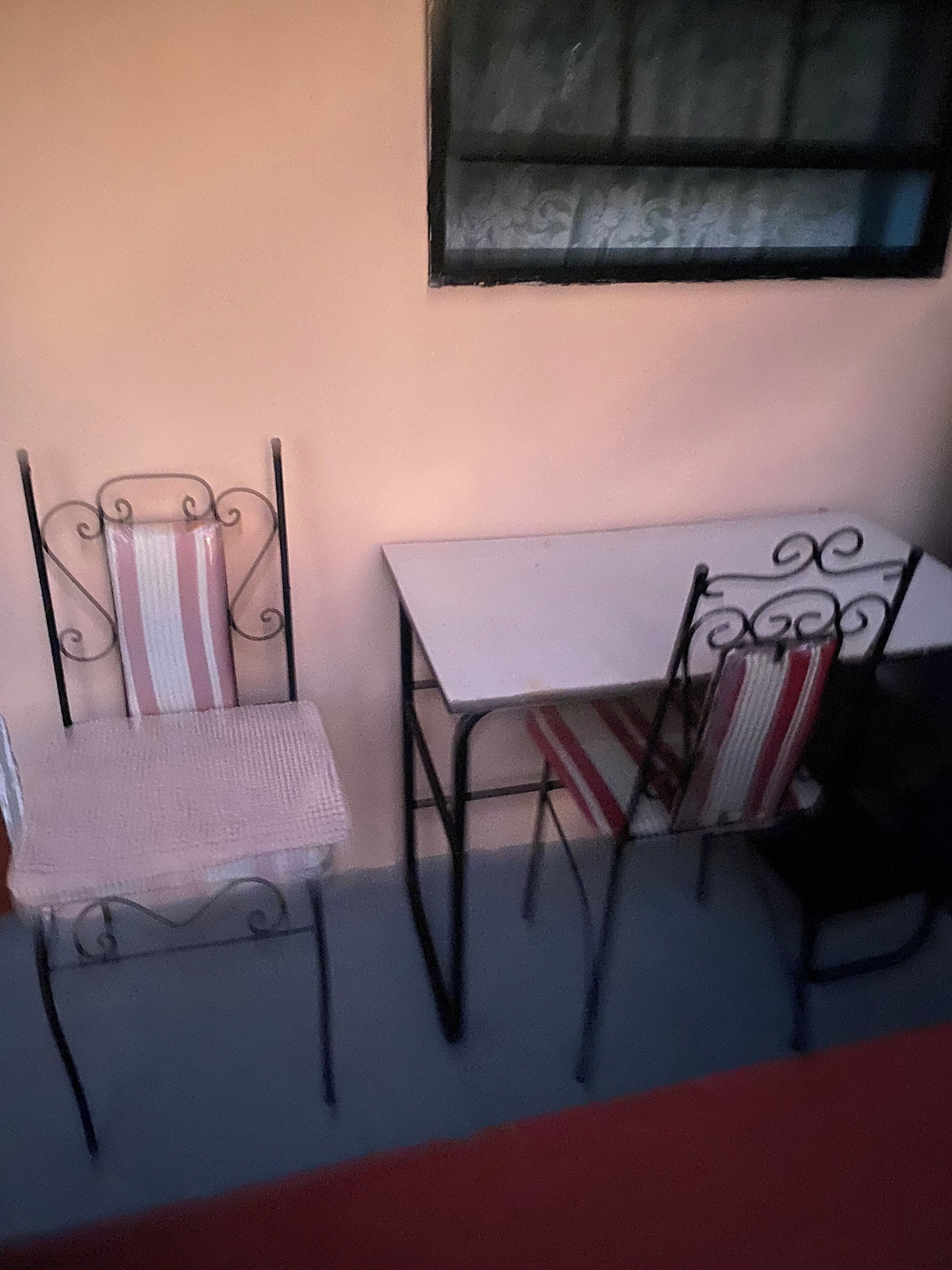 A small outdoor seating area with two metal chairs and a table, against a plain wall.