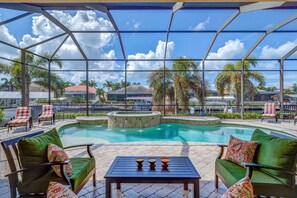 A pool area with lounge chairs and a table, surrounded by a glass enclosure with a view of palm trees and buildings.