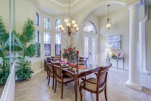 A dining area with a glass table, wooden chairs, and a chandelier.
