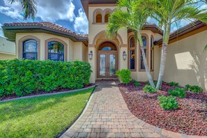 Stucco home with a central entrance, arched windows, and a tiled roof, set amidst lush greenery and a well-manicured lawn.