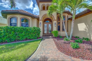 Stucco home with a central entrance, arched windows, and a tiled roof, set amidst lush greenery and a well-manicured lawn.