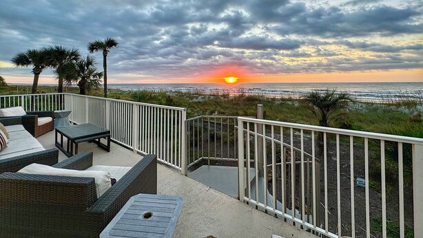 Un balcone con mobili in vimini e vista sull'oceano al tramonto.