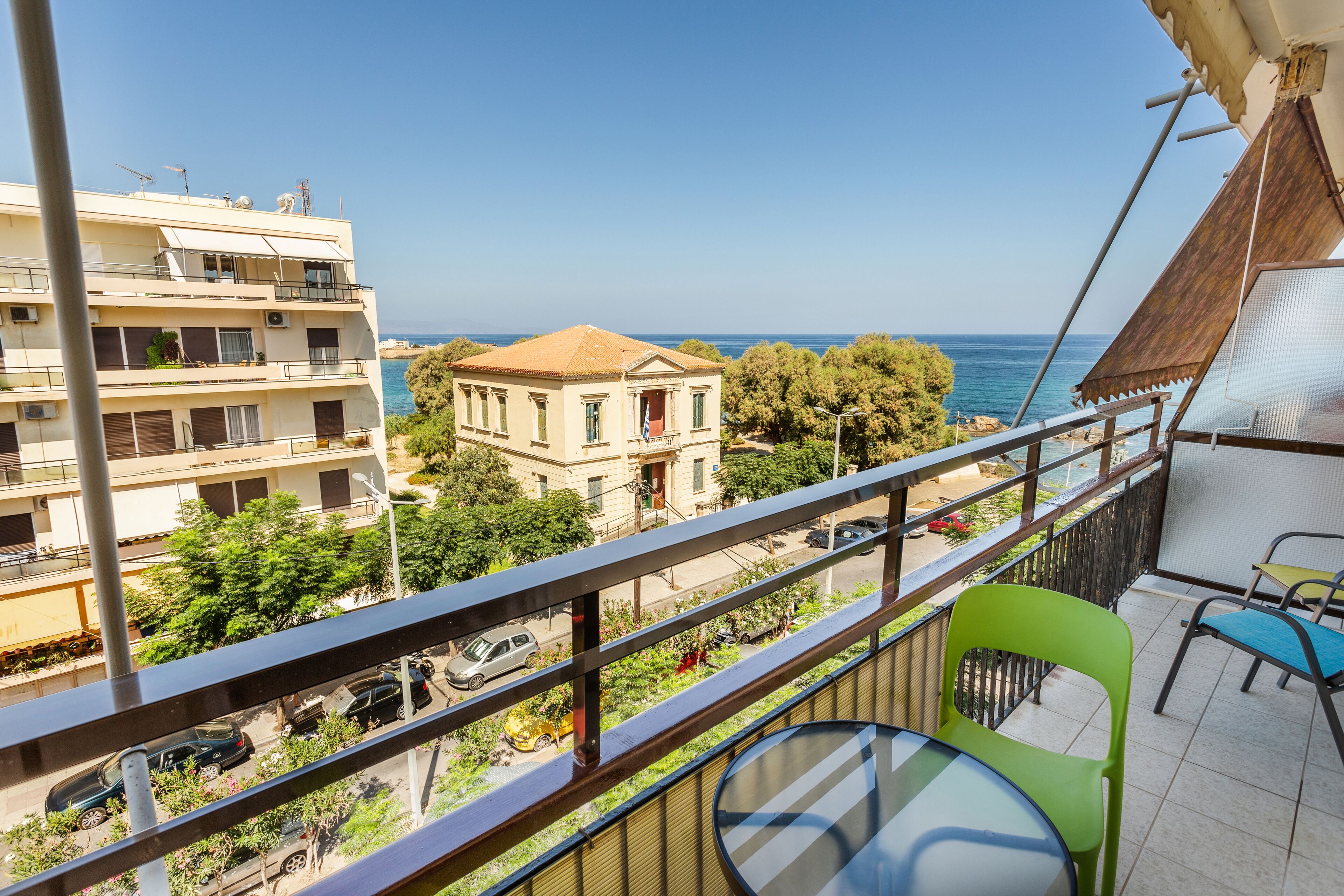Een balkon met uitzicht op zee, een gebouw met pannendak en een tafel met stoelen.
