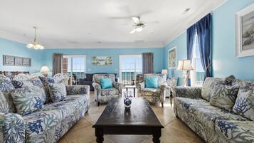 A living room with patterned sofas, a central coffee table, and a ceiling fan.
