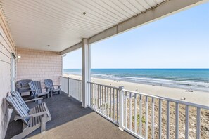 A covered balcony with Adirondack chairs, a view of the beach, and a white railing.