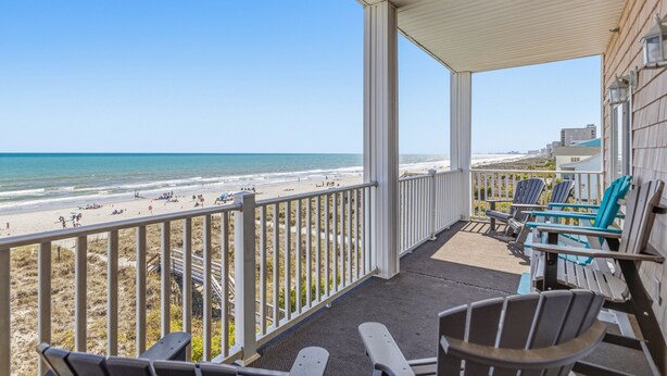 A balcony with a view of the beach, chairs, and a table.