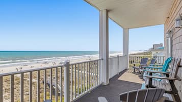 A balcony with a view of the beach, chairs, and a table.