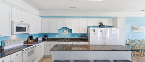 A modern kitchen with white cabinetry, a granite countertop, and a central island with bar stools.