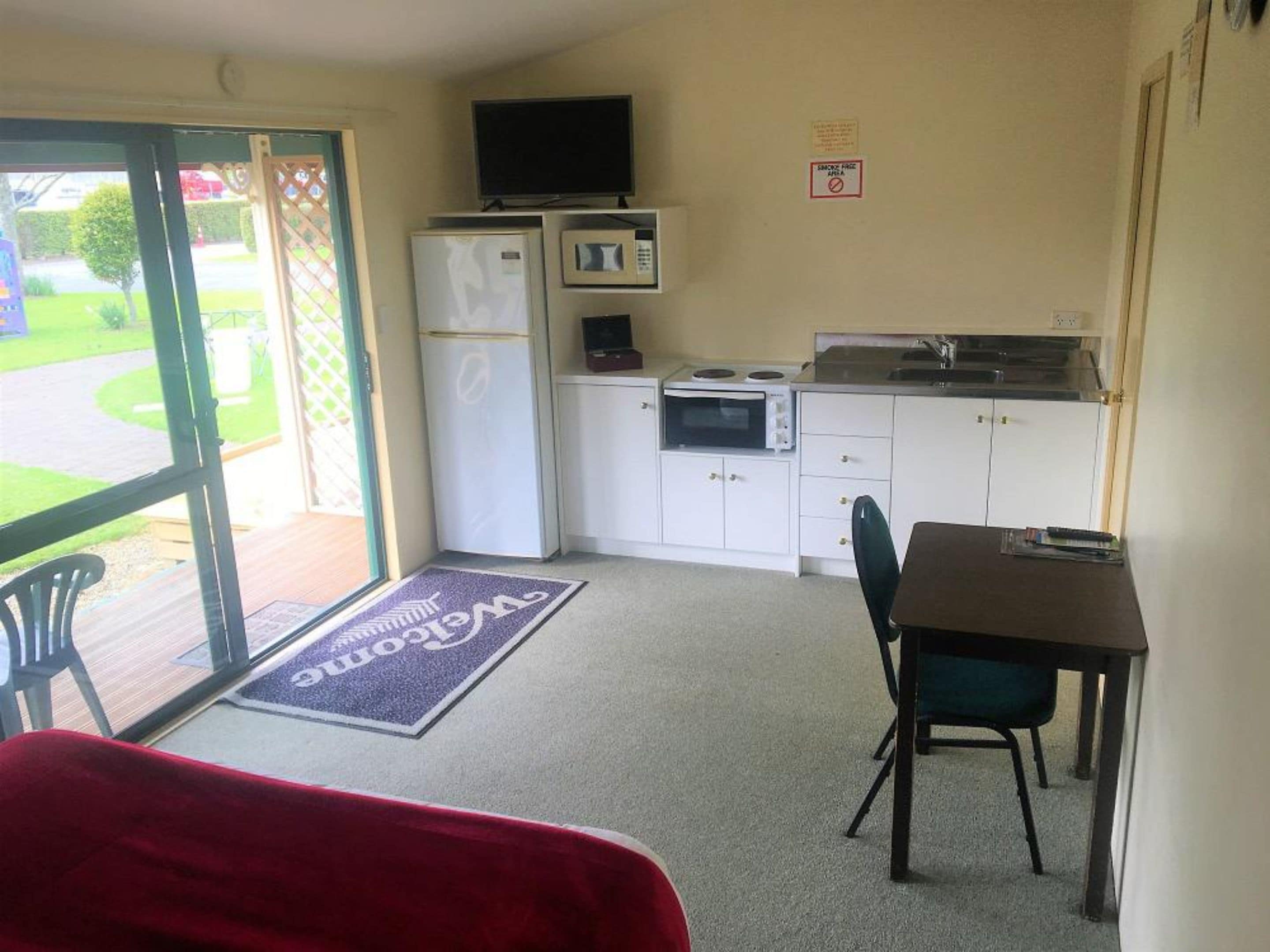A compact kitchenette with a refrigerator, microwave, and stove. There is a dining area with a table and chairs, and a red chair in the foreground.