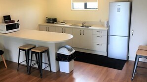 A compact kitchen with a central island, a microwave, a toaster, and a refrigerator. - Otorohanga Kiwi Holiday Park (Otorohanga)