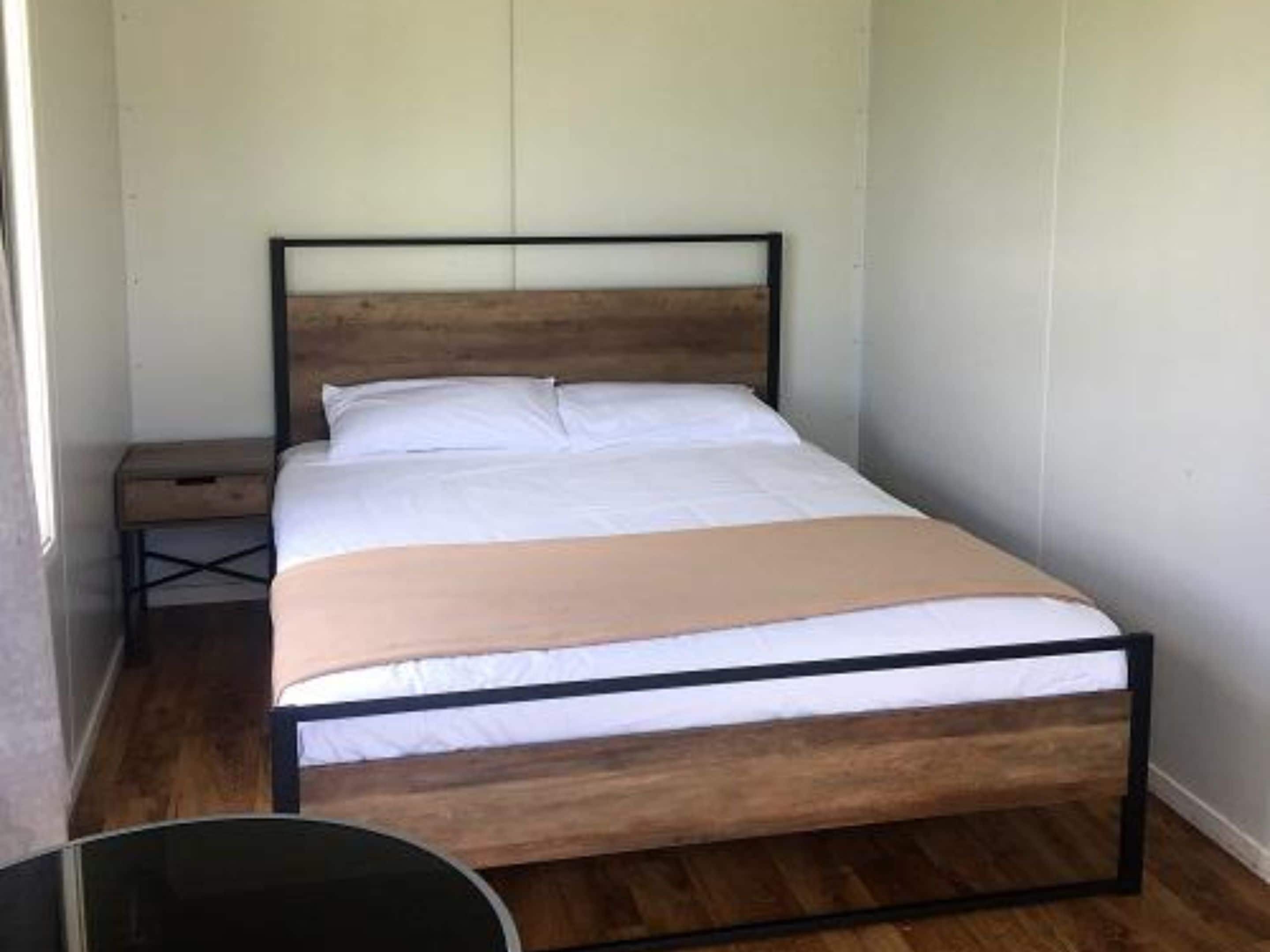 A single bed with a wooden headboard and a white mattress in a room with light-colored walls and wooden flooring.