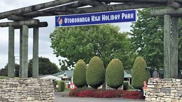 A sign for Otorohanga Kiwi Holiday Park with stone walls and neatly trimmed hedges.