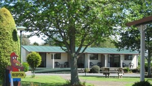 A reception area with a sign, a building with a green roof, and a pathway leading to the building. - Otorohanga Kiwi Holiday Park (Otorohanga)