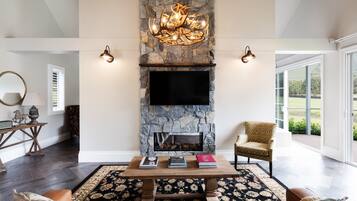 A living room with a stone fireplace, a flat-screen TV, a coffee table with books, a patterned rug, and a leather sofa.