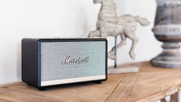 A Marshall speaker on a wooden table with a decorative horse and lamp in the background.