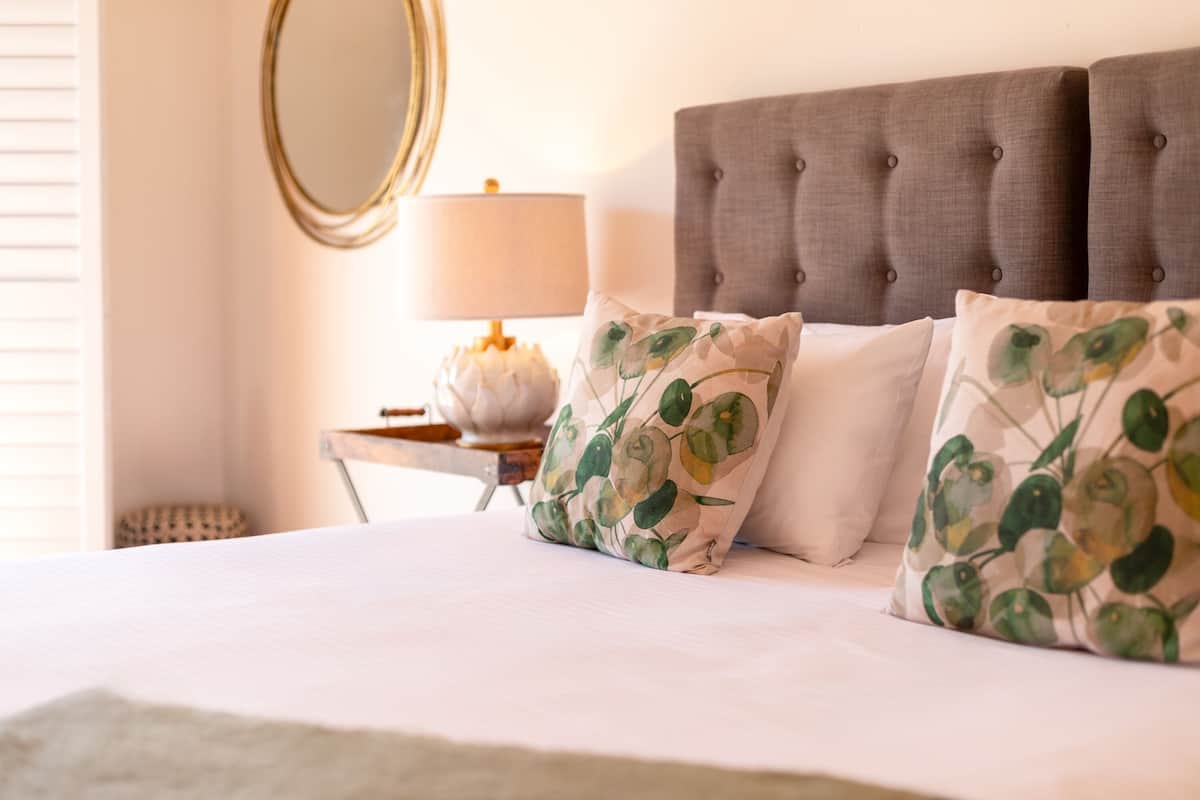 A neatly made bed with a tufted headboard, a bedside lamp, and a mirror on the wall.
