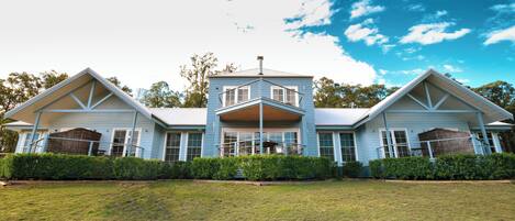 A two-story house with a central balcony, surrounded by a well-maintained lawn and hedges.