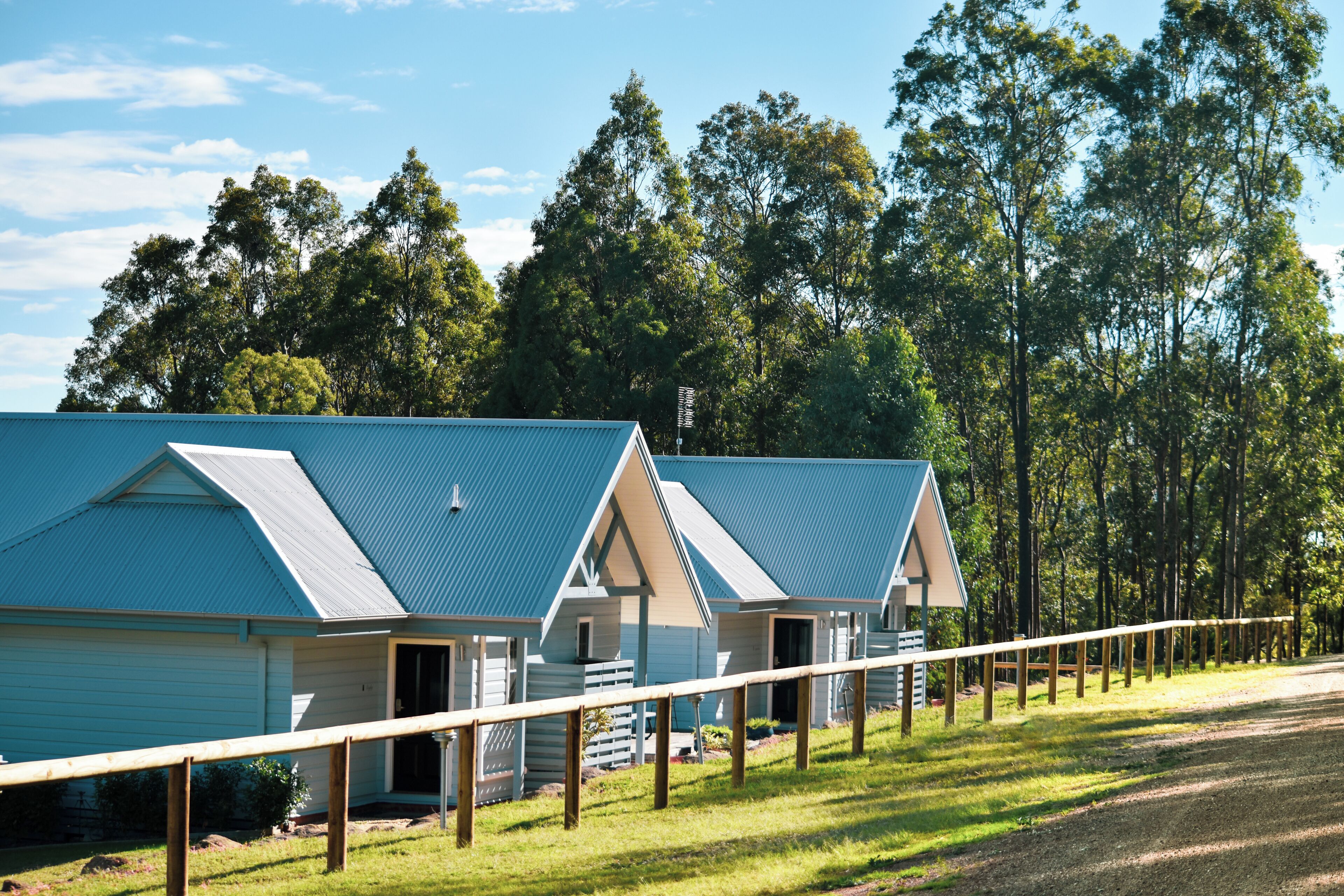 A row of blue-roofed cabins with a grassy area in front, surrounded by trees.