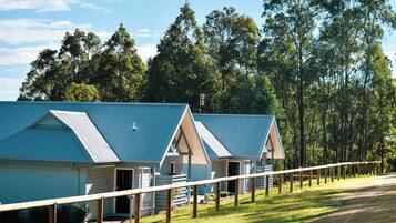A row of blue-roofed cabins with a grassy area in front, surrounded by trees.