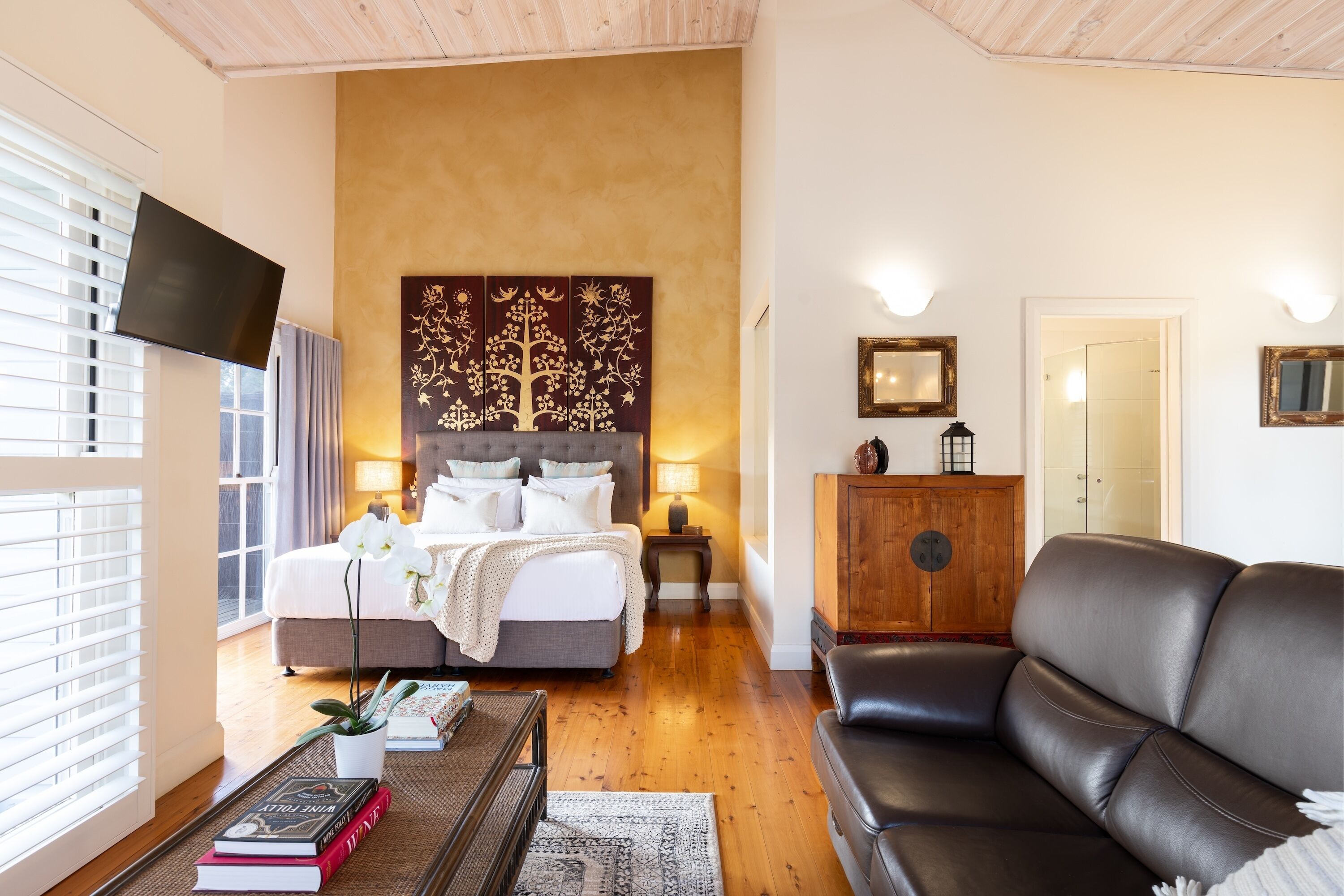 Une chambre à coucher avec un lit, des lampes de chevet, une télévision, une armoire en bois et un canapé en cuir.