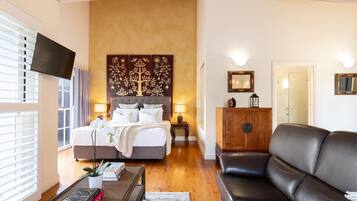 Une chambre à coucher avec un lit, des lampes de chevet, une télévision, une armoire en bois et un canapé en cuir.