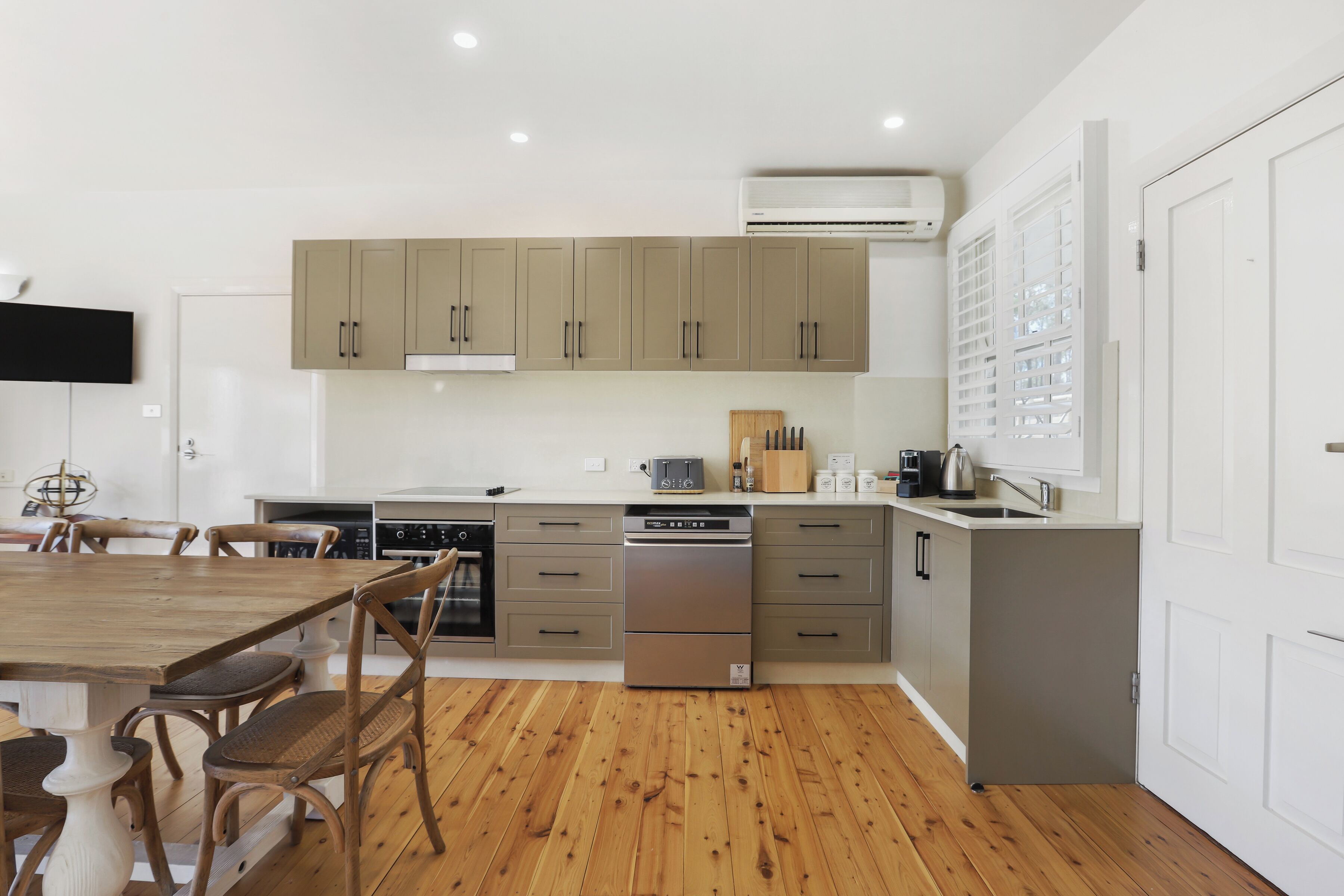 Una cocina moderna con suelo de madera, armarios empotrados, lavavajillas y un televisor de pantalla plana.