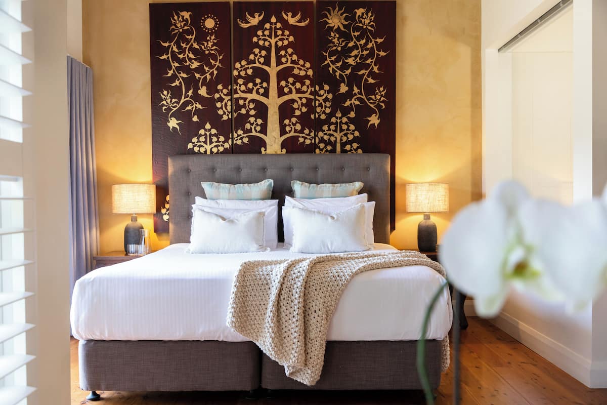A double bed with a grey headboard, two bedside lamps, and a decorative wall panel.