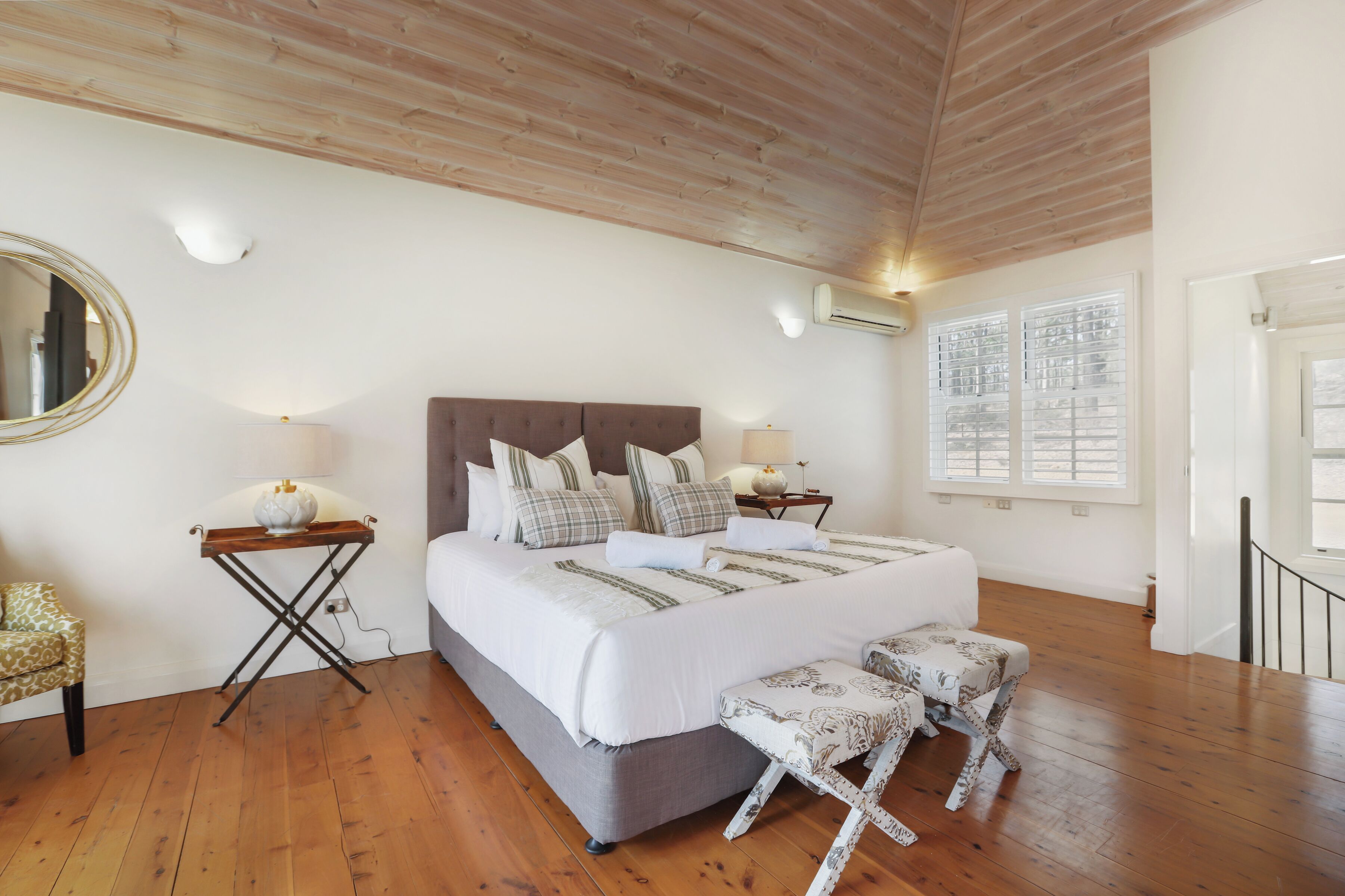 A bedroom with a large bed, bedside tables, a mirror, and a window with blinds.