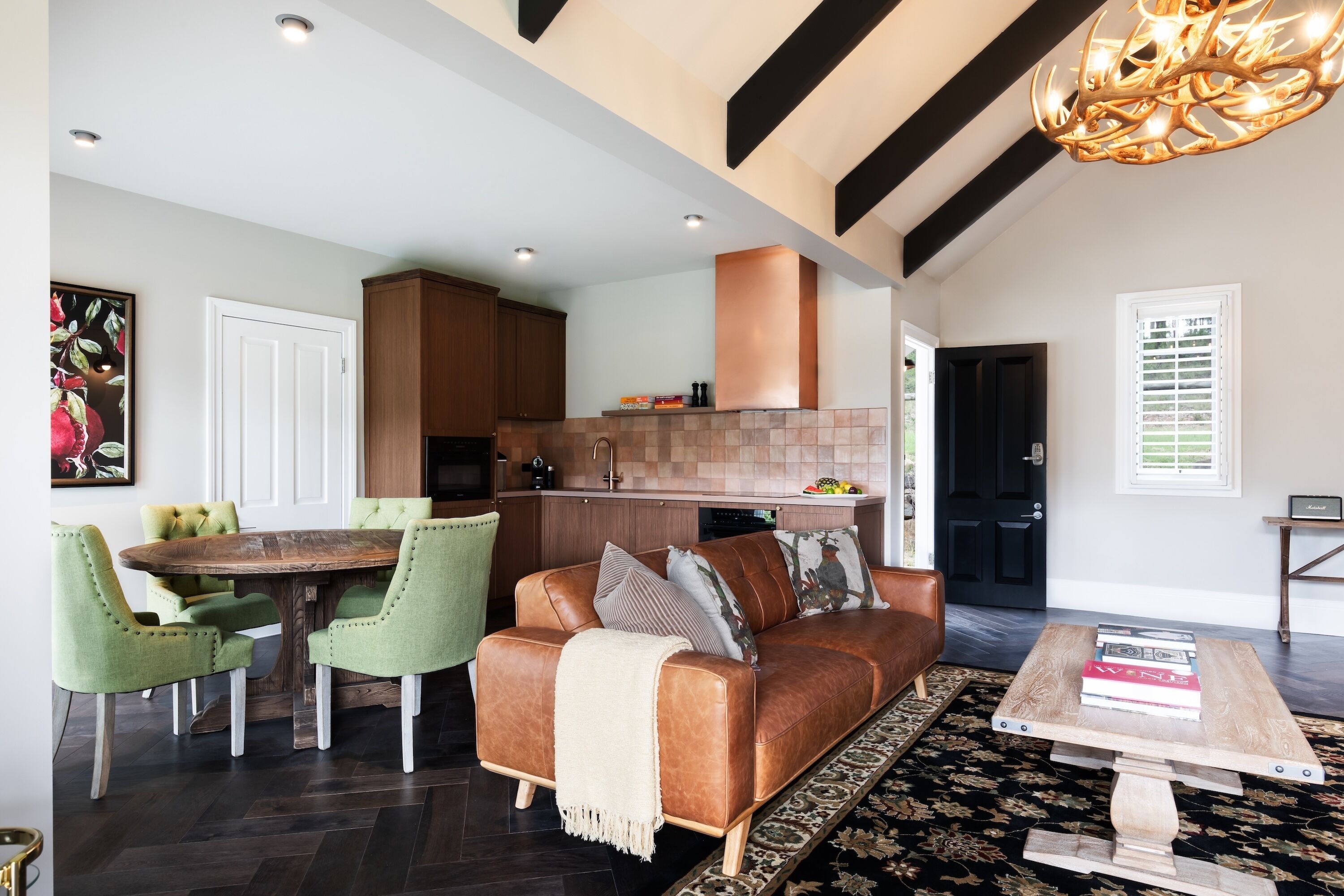 A spacious living area with a brown leather sofa, green armchairs, a wooden coffee table, and a dining table with chairs.