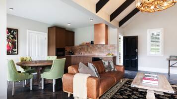 A spacious living area with a brown leather sofa, green armchairs, a wooden coffee table, and a dining table with chairs.