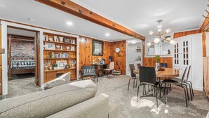 A cozy living room with a wooden ceiling, a dining table with chairs, a sofa, and a bookshelf filled with books and decorative items. - Clean, comfortable, spacious Fort Grounds apartment: great location!  (Coeur d'Alene)