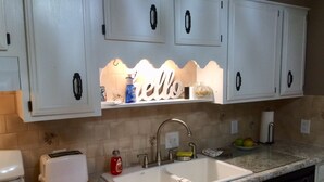 Una cucina con mobili bianchi, un lavello, un tostapane e un tagliere rosso.