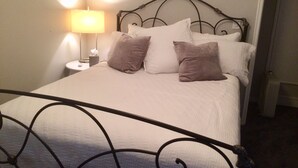Un letto rifatto con biancheria bianca e diversi cuscini, una lampada da comodino e un piccolo tavolo con un astuccio di fazzoletti.