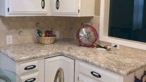 Una cucina con mobili bianchi, un piano di lavoro in granito, una ventola rossa e una finestra.