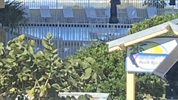 A beach view with lounge chairs and umbrellas, a fence, and a sign indicating a beach resort. - Best deal on the beach/sleeps 6/All New/Gulf views!/55 inch TV (Indian Shores)