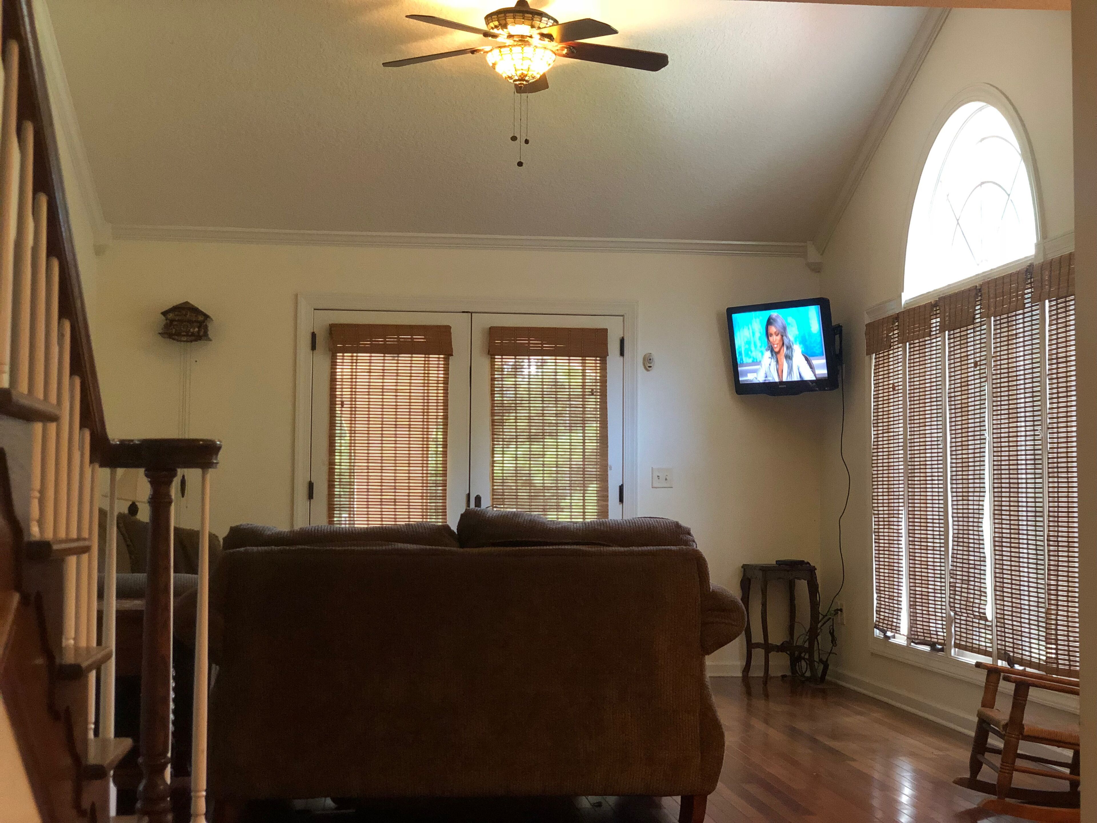 A living room with a ceiling fan, a television, and a large window with blinds.