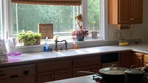 Una cocina con armarios de madera, una ventana con vista a follaje, un lavamanos y una estufa.