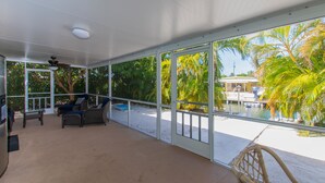 A spacious room with large windows, a ceiling fan, and a view of the beach and palm trees. - Waterfront & Privacy, Heated Pool  HotTub & waterfall, 60' Dock TikiHut, pets ok (Marathon)