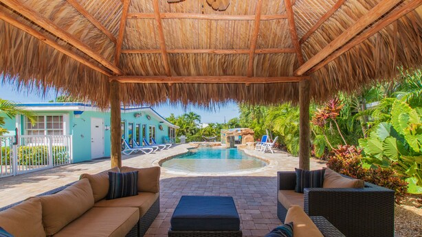 A covered outdoor area with a pool, lounge chairs, and a thatched roof. - Waterfront & Privacy, Heated Pool  HotTub & waterfall, 60' Dock TikiHut, pets ok (Marathon)
