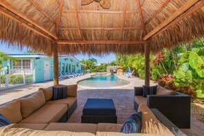 A covered outdoor area with a pool, lounge chairs, and a thatched roof. - Waterfront & Privacy, Heated Pool  HotTub & waterfall, 60' Dock TikiHut, pets ok (Marathon)