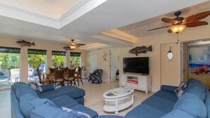 A spacious living room with a large sectional sofa, a television, and ceiling fans. - Waterfront & Privacy, Heated Pool  HotTub & waterfall, 60' Dock TikiHut, pets ok (Marathon)