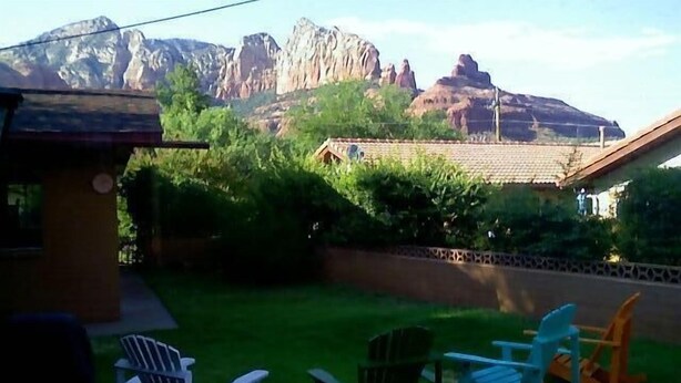 A backyard with a grassy lawn, several rocking chairs, and a mountain backdrop. - Great Location Best Value Beautiful House and Guest House with Views (Sedona)