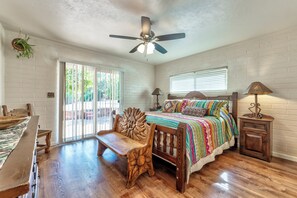 A bedroom with a bed, a ceiling fan, a window with blinds, a wooden bench, and a small table.