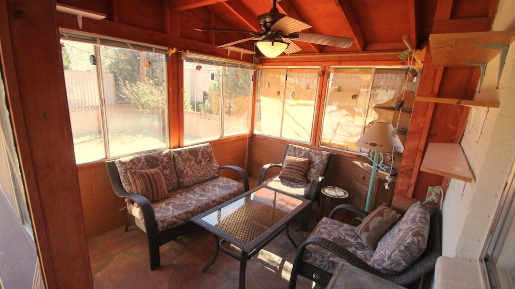 Une véranda avec un ventilateur de plafond, de grandes fenêtres, un canapé, une table basse et une lampe.