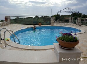 Relax by the oval-shaped pool surrounded by a deck and a shaded pergola.