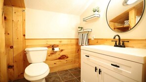 Une salle de bain avec un mur en bois, des toilettes blanches, un lavabo blanc avec un robinet noir et un miroir au-dessus du lavabo.