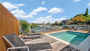 A rooftop pool area with lounge chairs, a wooden deck, and a view of the marina and buildings in the background.