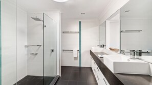 Een moderne badkamer met een douchecabine van glas, een grote spiegel en een zwart aanrecht met een witte wasbak.